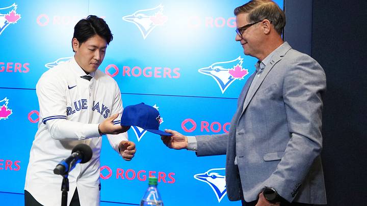 Jan 6, 2026; Toronto, Ontario, Canada; Toronto Blue Jays general manager Ross Atkins hands a baseball cap to Kazuma Okamoto during the press conference room at Rogers Centre. Mandatory Credit: Nick Turchiaro-Imagn Images