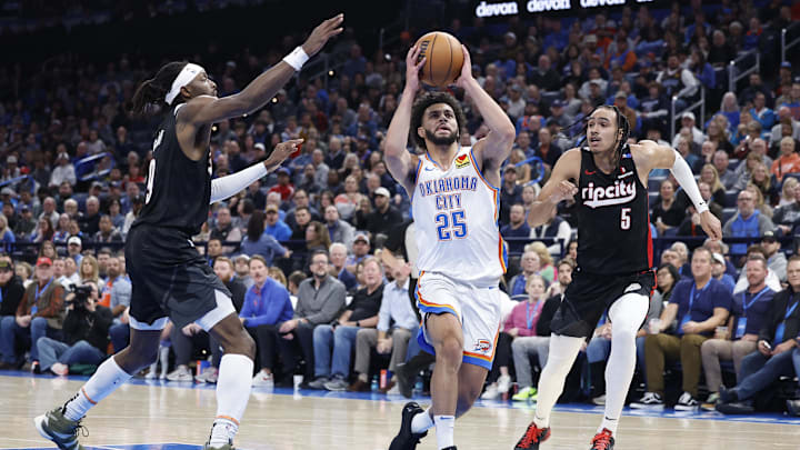Nov 20, 2024; Oklahoma City, Oklahoma, USA; Oklahoma City Thunder guard Ajay Mitchell (25) drives between Portland Trail Blazers forward Jerami Grant (9) and guard Dalano Banton (5) during the second half at Paycom Center. Mandatory Credit: Alonzo Adams-Imagn Images