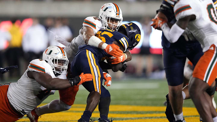 Oct 5, 2024; Berkeley, California, USA; Miami Hurricanes linebacker Raul Aguirre Jr. (center left) and defensive lineman Rueben Bain Jr. (left) tackle California Golden Bears running back Jaivian Thomas (center right) during the fourth quarter at California Memorial Stadium. Mandatory Credit: Darren Yamashita-Imagn Images