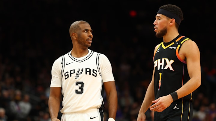 Dec 3, 2024; Phoenix, Arizona, USA; San Antonio Spurs guard Chris Paul (3) talks to Phoenix Suns guard Devin Booker (1) in the second half of an NBA Cup game at Footprint Center. Mandatory Credit: Mark J. Rebilas-Imagn Images