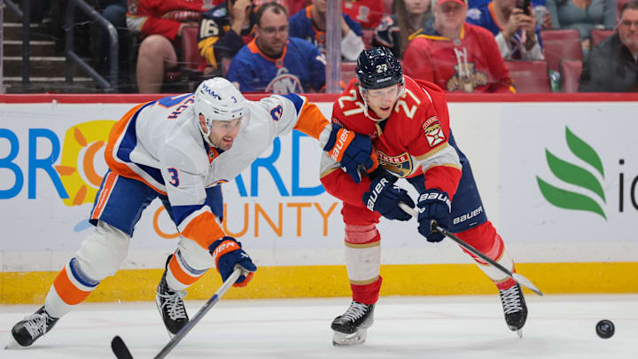 Dec 7, 2025; Sunrise, Florida, USA; Florida Panthers center Eetu Luostarinen (27) battles for the puck against New York Islanders defenseman Adam Pelech (3) during the second period at Amerant Bank Arena. Mandatory Credit: Sam Navarro-Imagn Images