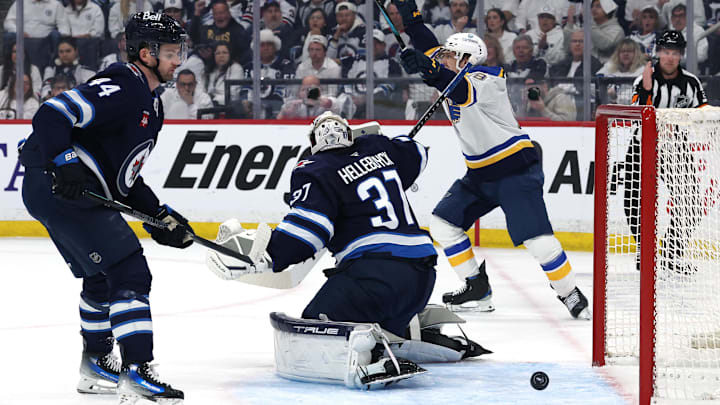 Apr 21, 2025; Winnipeg, Manitoba, CAN;St. Louis Blues right wing Jimmy Snuggerud (21) (not shown) score on Winnipeg Jets goaltender Connor Hellebuyck (37) as teammate St. Louis Blues center Robert Thomas (18) celebrates in the first period in game two of the first round of the 2025 Stanley Cup Playoffs at Canada Life Centre. Mandatory Credit: James Carey Lauder-Imagn Images