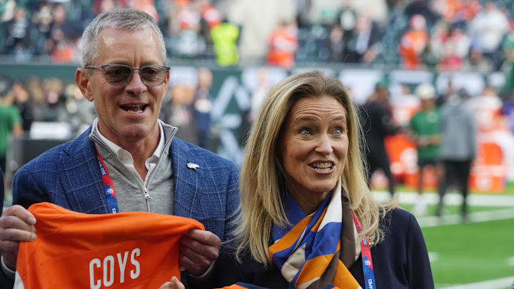Oct 12, 2025; Tottenham, United Kingdom; Denver Broncos co-owners Greg Penner and Claire Walton Penner pose with jerseys before an NFL International Series game against the New York Jets at Tottenham Hotspur Stadium. Mandatory Credit: Kirby Lee-Imagn Images