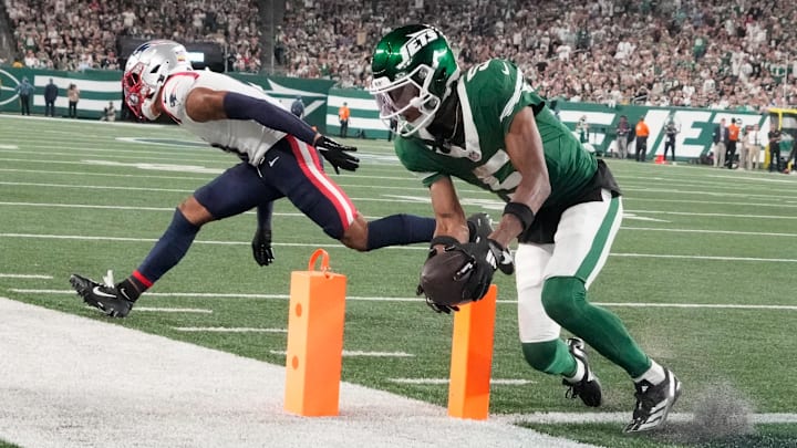 Sep 19, 2024; East Rutherford, New Jersey, USA;  New York Jets wide receiver Garrett Wilson (5)  scores a 3rd quarter touchdown in front of New England Patriots cornerback Christian Gonzalez (0)  at MetLife Stadium. 