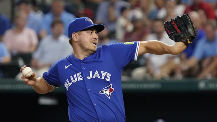 A baseball player in a blue jersey that says "Blue Jays" in white pitching a white baseball A baseball player in a blue jersey that says "Blue Jays" in white pitching a white baseball