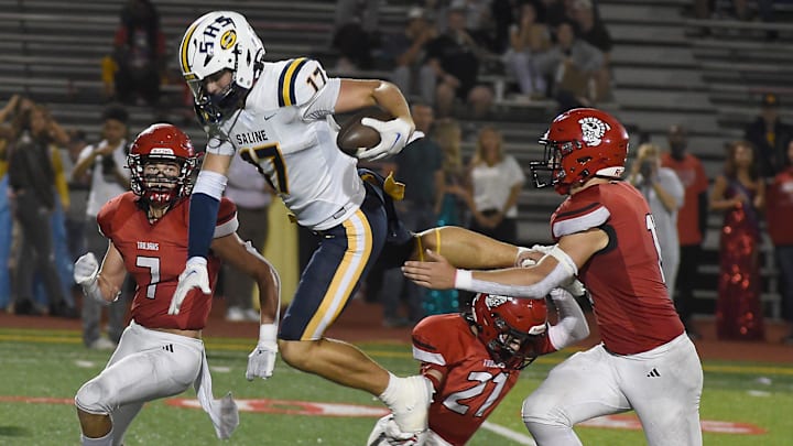 Lincoln Keyes of Saline is upended after a catch from number 21, Tanner Collett and Jax Jones (7) Friday, Sept. 20, 2024.