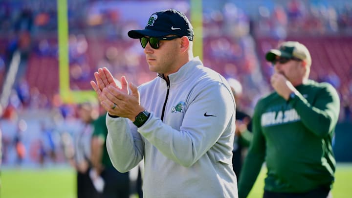 Tulane Green Wave coach Jon Sumrall claps hands at play in black hat grey jacket.