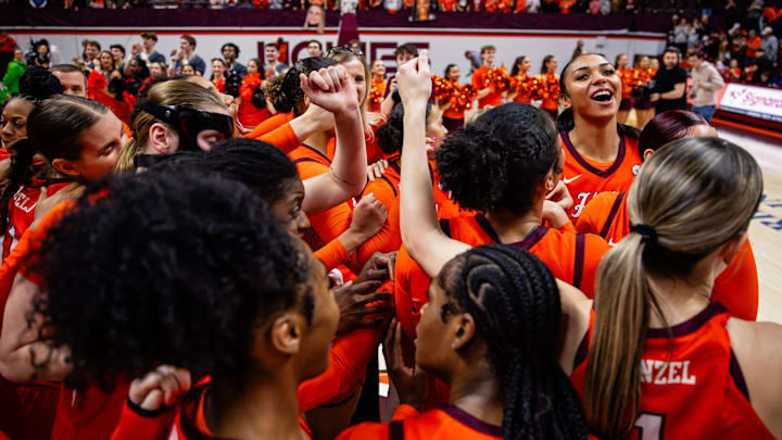 Virginia Tech Women's Basketball raises its hands in a huddle on the court. 