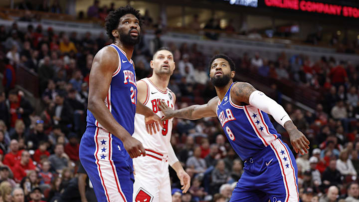 Dec 8, 2024; Chicago, Illinois, USA; Philadelphia 76ers center Joel Embiid (21) and forward Paul George (8) defend against Chicago Bulls center Nikola Vucevic (9) during the first half at United Center. Mandatory Credit: Kamil Krzaczynski-Imagn Images