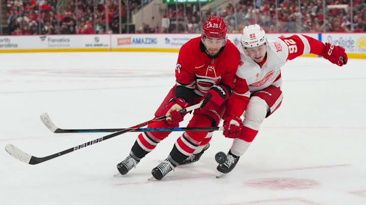Feb 28, 2026; Raleigh, North Carolina, USA;  Detroit Red Wings center Marco Kasper (92) and Carolina Hurricanes defenseman Sean Walker (26) chase after the puck during the first period at Lenovo Center. Mandatory Credit: James Guillory-Imagn Images