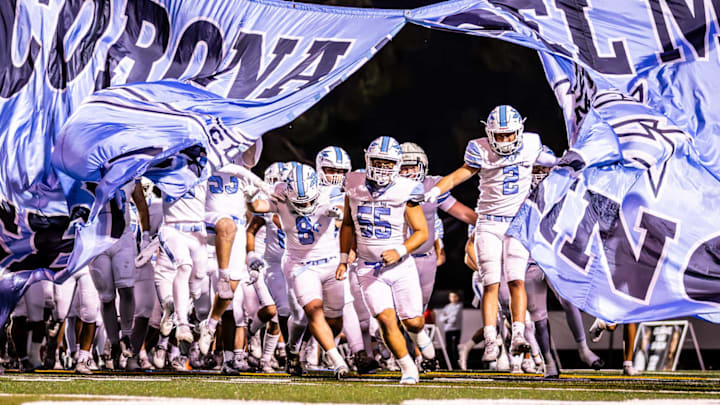 Corona del Mar football team bursts through a team banner before taking on Trabuco Hills.