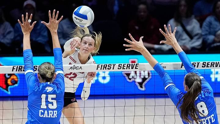 Wisconsin Badgers outside hitter Audrey Flanagan (22) attacks the ball as Kentucky Wildcats middle blocker Lizzie Carr (15) and Kentucky Wildcats outside hitter Morgan Gaerte (18) prepare to block during the second set of their match at the AVCA First Serve event at Fiserv Forum in Milwaukee, Wisconsin on Aug. 21, 2026.