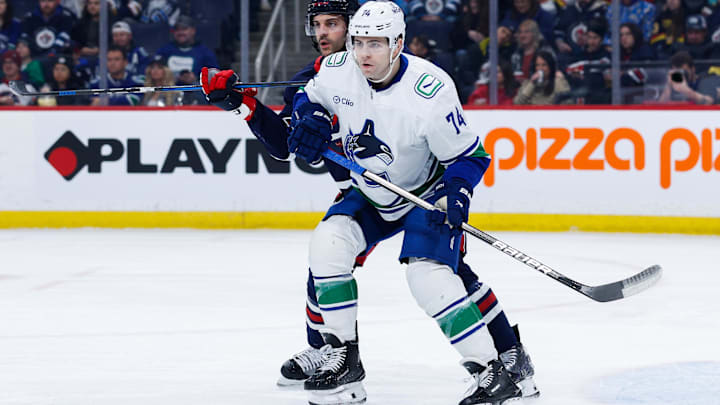 Jan 14, 2025; Winnipeg, Manitoba, CAN;  Vancouver Canucks forward Jake DeBrusk (74) and Winnipeg Jets defenseman Dylan DeMelo (2) look for the puck during the first period at Canada Life Centre. Mandatory Credit: Terrence Lee-Imagn Images