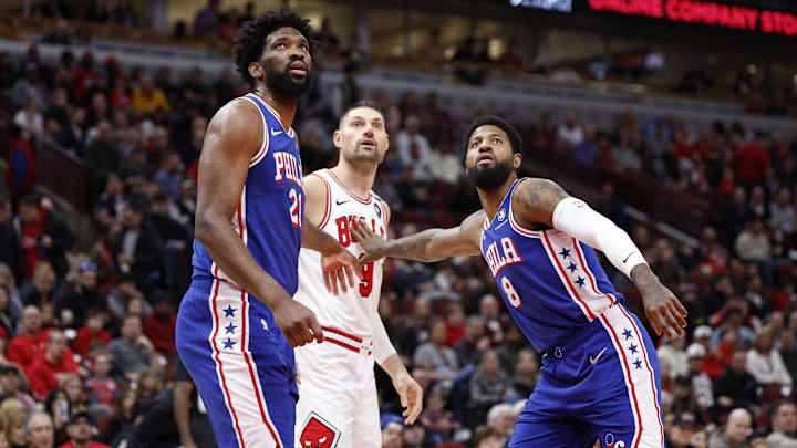 Dec 8, 2024; Chicago, Illinois, USA; Philadelphia 76ers center Joel Embiid (21) and forward Paul George (8) defend against Chicago Bulls center Nikola Vucevic (9) during the first half at United Center. Mandatory Credit: Kamil Krzaczynski-Imagn Images