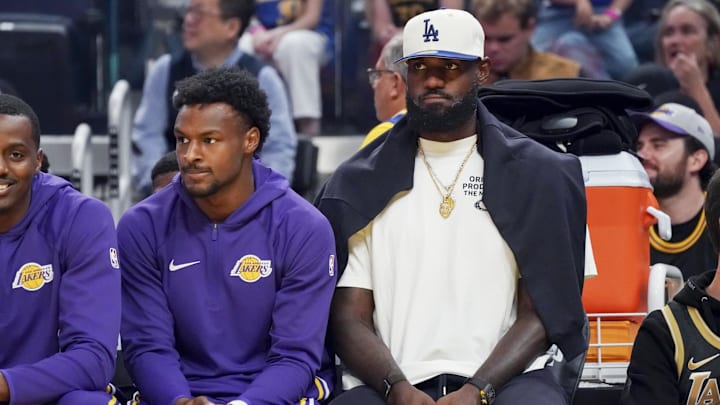 Oct 5, 2025; San Francisco, California, USA; Los Angeles Lakers guard Bronny James (9) and forward LeBron James (23), wearing a Los Angeles Dodgers cap, watch the action against the Golden State Warriors in the first quarter at Chase Center. Mandatory Credit: David Gonzales-Imagn Images Oct 5, 2025; San Francisco, California, USA; Los Angeles Lakers guard Bronny James (9) and forward LeBron James (23), wearing a Los Angeles Dodgers cap, watch the action against the Golden State Warriors in the first quarter at Chase Center. Mandatory Credit: David Gonzales-Imagn Images