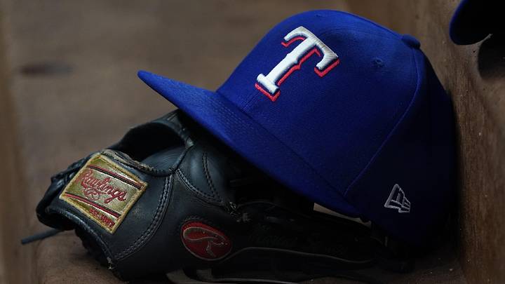A Texas Rangers hat sits on top of a player's glove in the dugout.