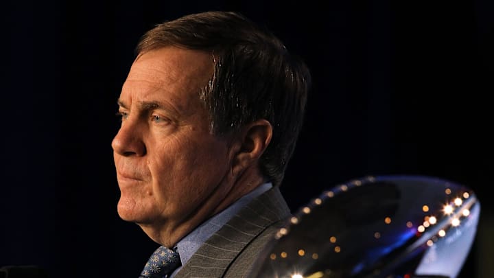 2012: The Vince Lombardi Trophy with Patriots and Giants team helmets shine in the foreground as Patriots head coach Bill Belichick listens to a question during his press conference at the Media Center.
