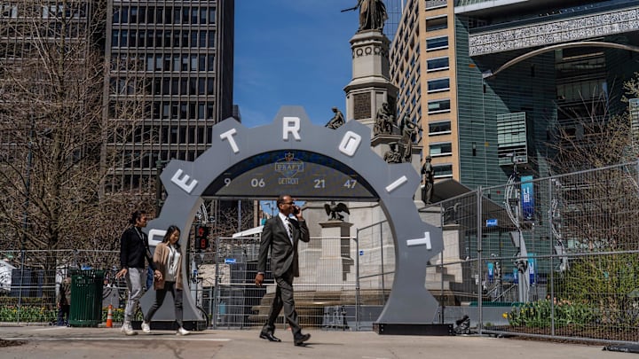 People walk past the countdown clock as work continues on the setup for the upcoming NFL Draft near