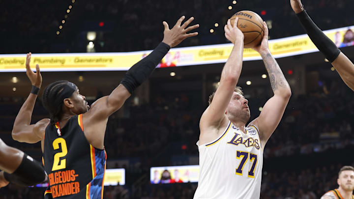 Apr 6, 2025; Oklahoma City, Oklahoma, USA; Los Angeles Lakers guard Luka Doncic (77) drives to the basket between Oklahoma City Thunder guard Shai Gilgeous-Alexander (2) and forward Jalen Williams (8) during the second quarter at Paycom Center. Mandatory Credit: Alonzo Adams-Imagn Images