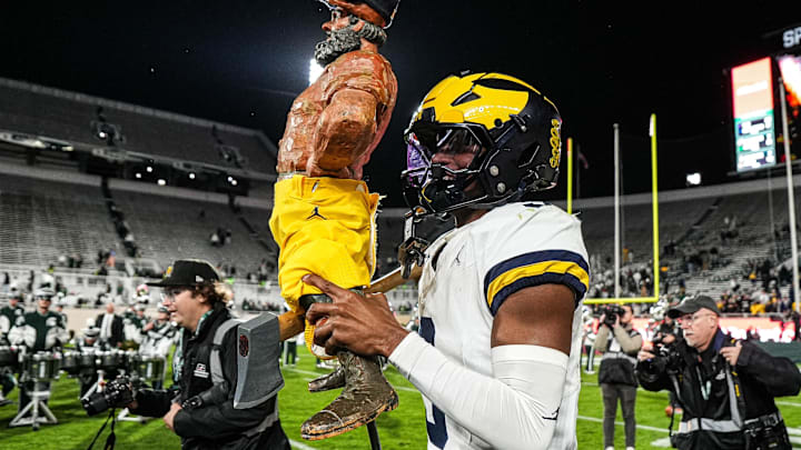 Michigan defensive back Jaden Mangham (3) holds up the the Paul Bunyan Trophy 