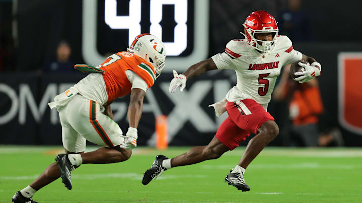 Oct 17, 2025; Miami Gardens, Florida, USA; Louisville Cardinals wide receiver Caullin Lacy (5) carries the football against Miami Hurricanes safety Zechariah Poyser (7) during the first quarter at Hard Rock Stadium. Mandatory Credit: Sam Navarro-Imagn Images Oct 17, 2025; Miami Gardens, Florida, USA; Louisville Cardinals wide receiver Caullin Lacy (5) carries the football against Miami Hurricanes safety Zechariah Poyser (7) during the first quarter at Hard Rock Stadium. Mandatory Credit: Sam Navarro-Imagn Images