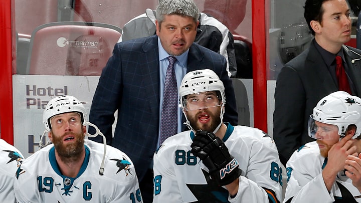 Head coach Todd McLellan stands over Joe Thornton (19) and Brent Burns (88) on the bench.