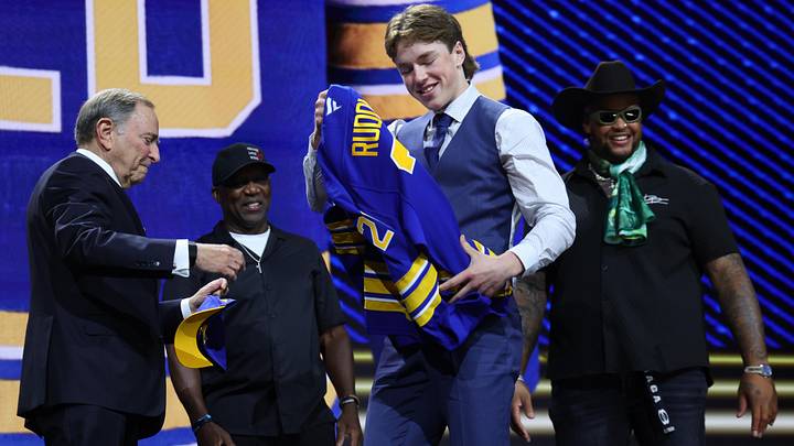 Jun 26, 2026; Buffalo, New York, USA; Daxon Rudolph takes a sweater from NHL commissioner Gary Bettman in front of former Buffalo Bills player Thurman Thomas and current Bills player Dion Dawkins watch after being selected with the fourth pick in the first round of the 2026 NHL Draft by the Buffalo Sabres at KeyBank Center. Mandatory Credit: Timothy T. Ludwig-Imagn Images