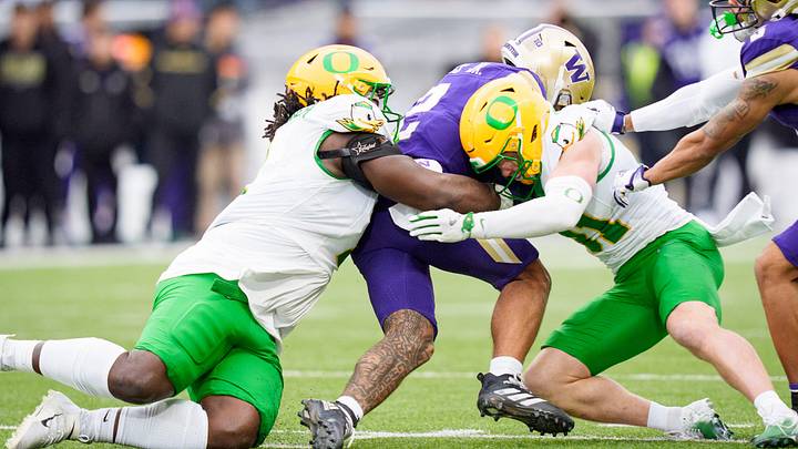 Oregon defensive lineman Bear Alexander, left, and Oregon defensive back Dillon Thieneman bring down Washington quarterback Demond Williams Jr. as the Oregon Ducks take on the Washington Huskies on Nov. 29, 2025, at Husky Stadium in Seattle, Washington.