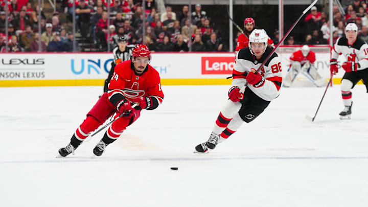 Dec 28, 2024; Raleigh, North Carolina, USA;  Carolina Hurricanes center Seth Jarvis (24) and New Jersey Devils center Jack Hughes (86) skate after the puck during the first period at Lenovo Center. Mandatory Credit: James Guillory-Imagn Images