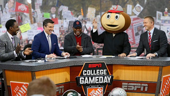 Lee Corso waves while wearing a Brutus Buckeye head as, from left, Desmond Howard, Rece Davis, Archie Griffin, and Kirk Herbstreit applaud his pick during ESPN's College GameDay broadcast from the campus of Ohio State prior to the NCAA football game against the Michigan State Spartans in Columbus on Nov. 21, 2015.