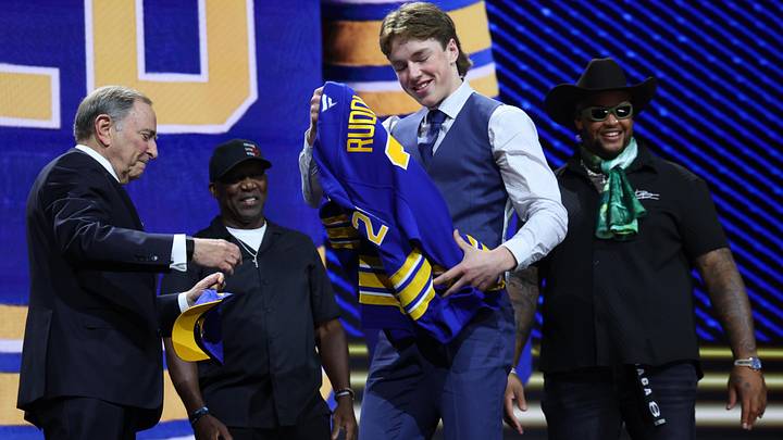 Jun 26, 2026; Buffalo, New York, USA; Daxon Rudolph takes a sweater from NHL commissioner Gary Bettman in front of former Buffalo Bills player Thurman Thomas and current Bills player Dion Dawkins watch after being selected with the fourth pick in the first round of the 2026 NHL Draft by the Buffalo Sabres at KeyBank Center. Mandatory Credit: Timothy T. Ludwig-Imagn Images