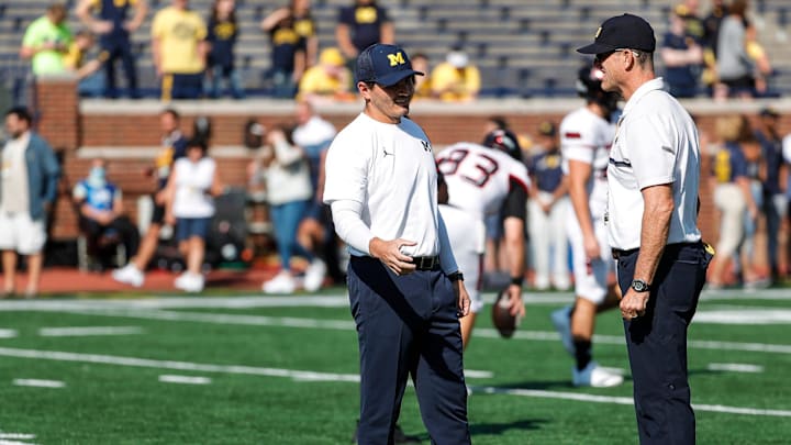 Michigan defensive coordinator Mike Macdonald, left, talks to head coach Jim Harbaugh during warmups