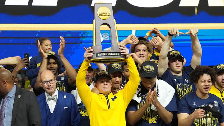 Apr 6, 2026; Indianapolis, IN, USA; Michigan Wolverines head coach Dusty May hoists the trophy after defeating the Connecticut Huskies in the national championship of the Final Four of the men's 2026 NCAA Tournament at Lucas Oil Stadium. Mandatory Credit: Robert Deutsch-Imagn Images