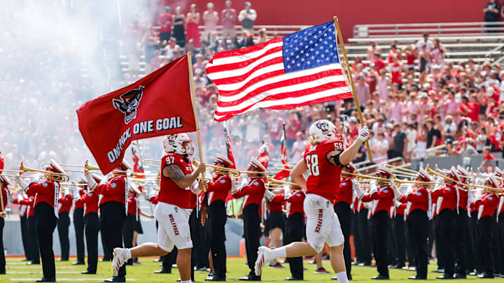 Sep 6, 2025; Raleigh, North Carolina, USA; North Carolina State Wolfpack defensive end Colby Cronk (58) runs with the American flag while defensive lineman Joseph Castaneda (97) runs with North Carolina State Wolfpack flag before the first half of the game against the Virginia Cavaliers at Carter-Finley Stadium. Mandatory Credit: Jaylynn Nash-Imagn Images