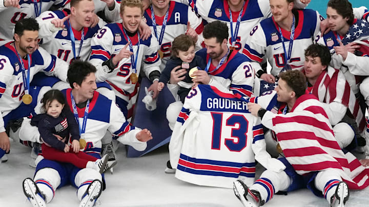 Feb 22, 2026; Milan, Italy; Zach Werenski (bottom left) of the United States celebrates while holding Noa Gaudreau, the daughter of the late Johnny Gaudreau while Dylan Larkin (21) holds Johnny Gaudreau Jr after winning the men's ice hockey gold medal game during the Milano Cortina 2026 Olympic Winter Games at Milano Santagiulia Ice Hockey Arena. Mandatory Credit: James Lang-Imagn Images