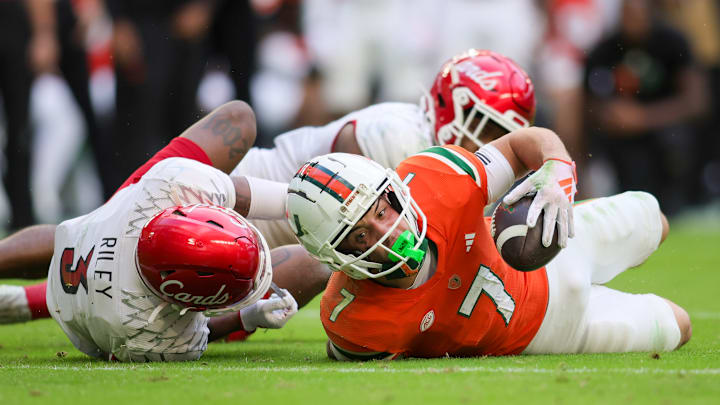 Nov 18, 2023; Miami Gardens, Florida, USA; Miami Hurricanes wide receiver Xavier Restrepo (7) is tackled short of the end zone by Louisville Cardinals defensive back Quincy Riley (3) during the fourth quarter at Hard Rock Stadium. Mandatory Credit: Sam Navarro-Imagn Images