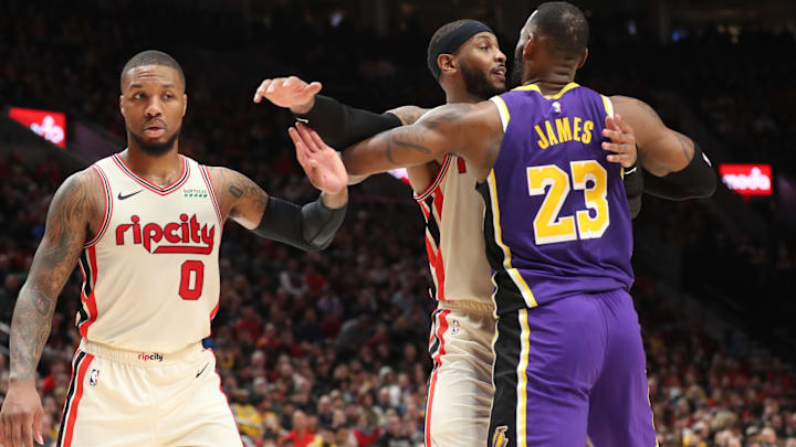 Dec 28, 2019; Portland, Oregon, USA; Portland Trail Blazers guard Damian Lillard (0) raises his hand as teammate Trail Blazers' forward Carmelo Anthony (00) holds Los Angeles Lakers forward LeBron James (23) in the second half at Moda Center. Mandatory Credit: Jaime Valdez-Imagn Images