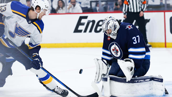 Apr 30, 2025; Winnipeg, Manitoba, CAN; Winnipeg Jets goalie Connor Hellebuyck (37) makes a save as St. Louis Blues forward Alexey Toropchenko (13) looks for a rebound during the first period in game five of the first round of the 2025 Stanley Cup Playoffs at Canada Life Centre. Mandatory Credit: Terrence Lee-Imagn Images