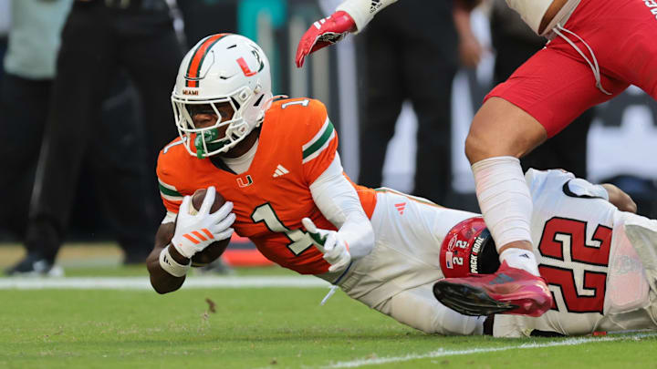 Nov 15, 2025; Miami Gardens, Florida, USA; Miami Hurricanes wide receiver Joshisa Trader (1) carries the football against NC State Wolfpack defensive back Jackson Vick (22) during the second quarter at Hard Rock Stadium. Mandatory Credit: Sam Navarro-Imagn Images