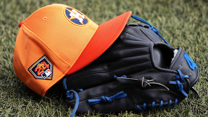 A Houston Astros hat sits on top of a baseball glove sitting on the grass.