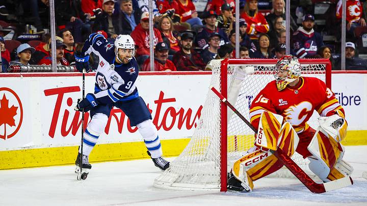 Nov 15, 2025; Calgary, Alberta, CAN; Winnipeg Jets left wing Alex Iafallo (9) controls the puck behind Calgary Flames goaltender Dustin Wolf (32) during the third period at Scotiabank Saddledome. Mandatory Credit: Sergei Belski-Imagn Images