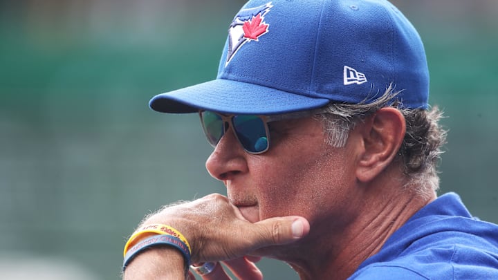 Toronto Blue Jays bench coach Don Mattingly holds his hand up to his mouth in sunglasses and a blue hat. Toronto Blue Jays bench coach Don Mattingly holds his hand up to his mouth in sunglasses and a blue hat.