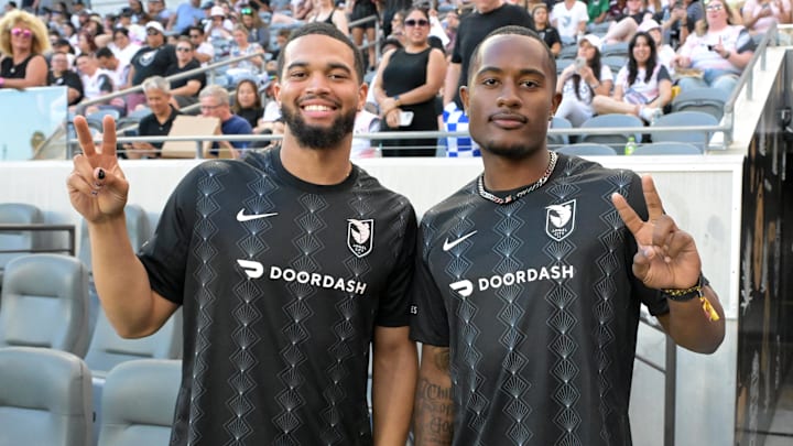 Bears QB Caleb Williams and former USC teammate, wide receiver Kyron Hudson, look on during a women's pro soccer matchup.