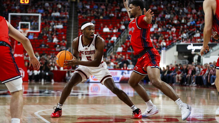 Dec 6, 2025; Raleigh, North Carolina, USA; NC State Wolfpack guard Tre Holloman (5) with the ball goaded by Liberty Flames guard JJ Harper (9) during the first half of the game at Lenovo Center. Mandatory Credit: Jaylynn Nash-Imagn Images