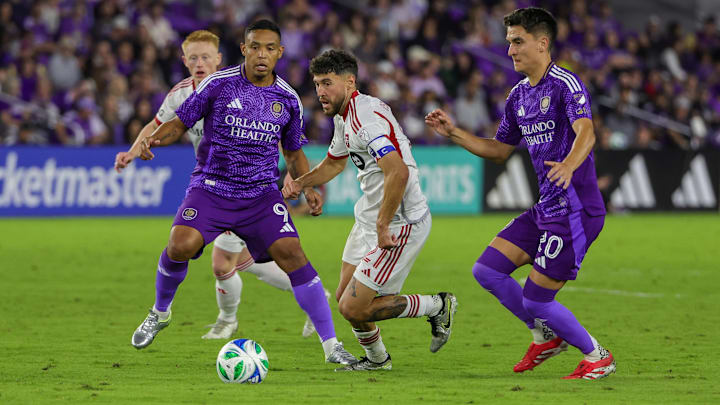 Mar 1, 2025; Orlando, Florida, USA; Toronto FC midfielder Jonathan Osorio (21) moves the ball against Orlando City forward Luis Muriel (9) and midfielder Eduard Atuesta (20) during the second half at Inter&Co Stadium. Mandatory Credit: Mike Watters-Imagn Images