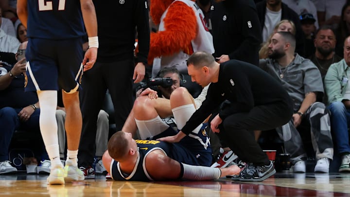 Dec 29, 2025; Miami, Florida, USA; Denver Nuggets center Nikola Jokic (15) grabs his left knee as head coach David Adelman approaches him after an injury against the Miami Heat during the second quarter at Kaseya Center. Mandatory Credit: Sam Navarro-Imagn Images Dec 29, 2025; Miami, Florida, USA; Denver Nuggets center Nikola Jokic (15) grabs his left knee as head coach David Adelman approaches him after an injury against the Miami Heat during the second quarter at Kaseya Center. Mandatory Credit: Sam Navarro-Imagn Images