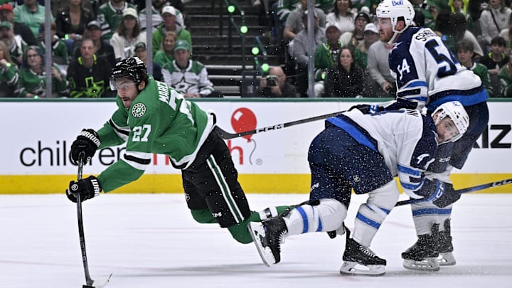 May 11, 2025; Dallas, Texas, USA; Dallas Stars left wing Mason Marchment (27) is tripped up as he shoots the puck past Winnipeg Jets defenseman Neal Pionk (4) and defenseman Dylan Samberg (54) during the second period in game three of the second round of the 2025 Stanley Cup Playoffs at American Airlines Center. Mandatory Credit: Jerome Miron-Imagn Images