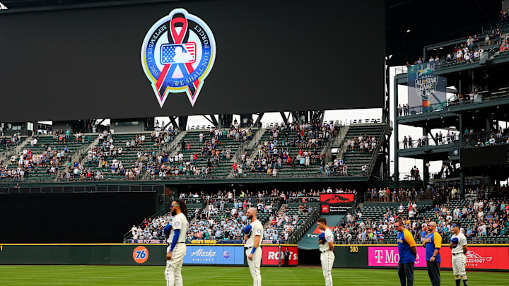 Sep 11, 2022; Seattle, Washington, USA;  An MLB logo with a graphic remembering the September 11th terrorist attacks is shown on the video screen as Seattle Mariners players hold their hats before the game against Atlanta Braves at T-Mobile Park. The Mariners beat the Braves 8-7. Mandatory Credit: Lindsey Wasson-Imagn Images
