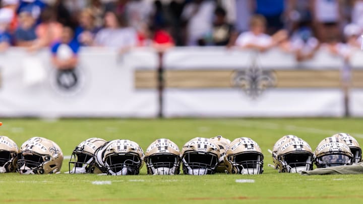 Jun 10, 2025; New Orleans, LA, USA; Detailed view of Saints helmets lined up with fans in the background during minicamp at Ochsner Sports Performance Center. Mandatory Credit: Stephen Lew-Imagn Images Jun 10, 2025; New Orleans, LA, USA; Detailed view of Saints helmets lined up with fans in the background during minicamp at Ochsner Sports Performance Center. Mandatory Credit: Stephen Lew-Imagn Images
