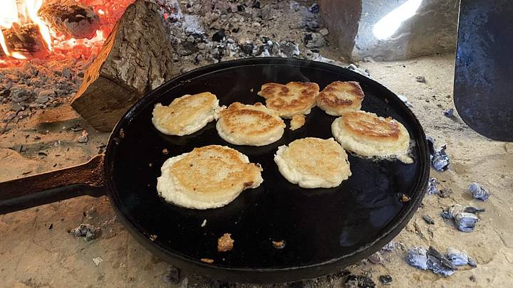 Hoecakes sizzling on a cast-iron griddle over an open hearth fire. Hoecakes sizzling on a cast-iron griddle over an open hearth fire.